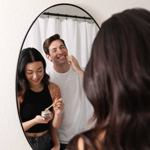 A couple using Wonder tooth whitening powder in a mirror