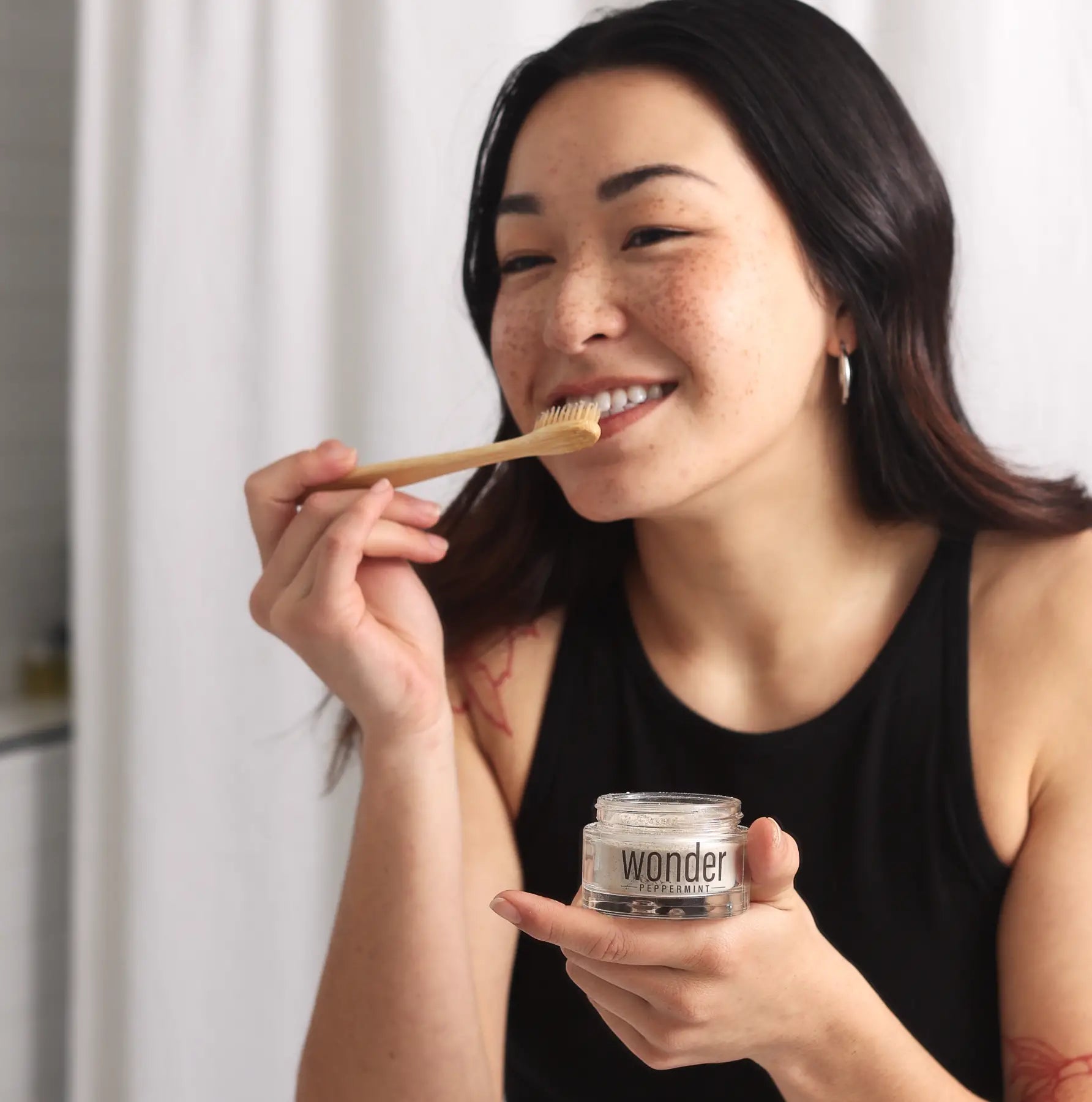Woman using Wonder peppermint tooth powder with a bamboo toothbrush