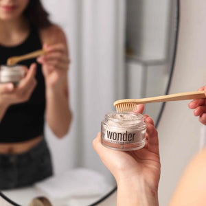 Woman applying Wonder peppermint tooth powder to a bamboo toothbrush