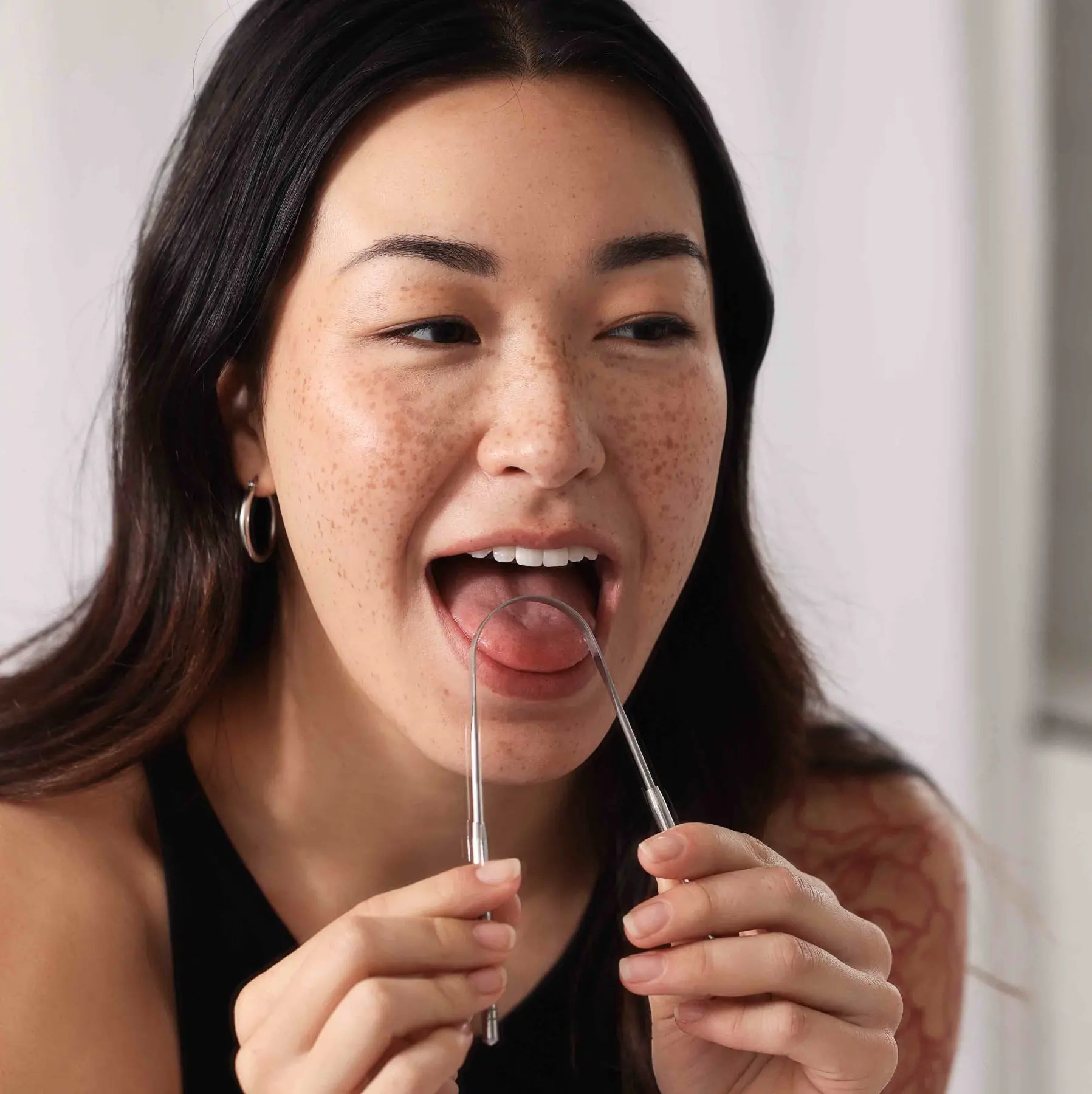 Woman using surgical-grade, stainless steel Wonder tongue cleaner