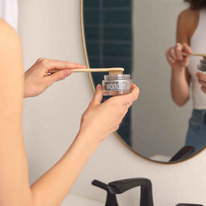 Woman applying Wonder whitening tooth powder to a bamboo toothbrush